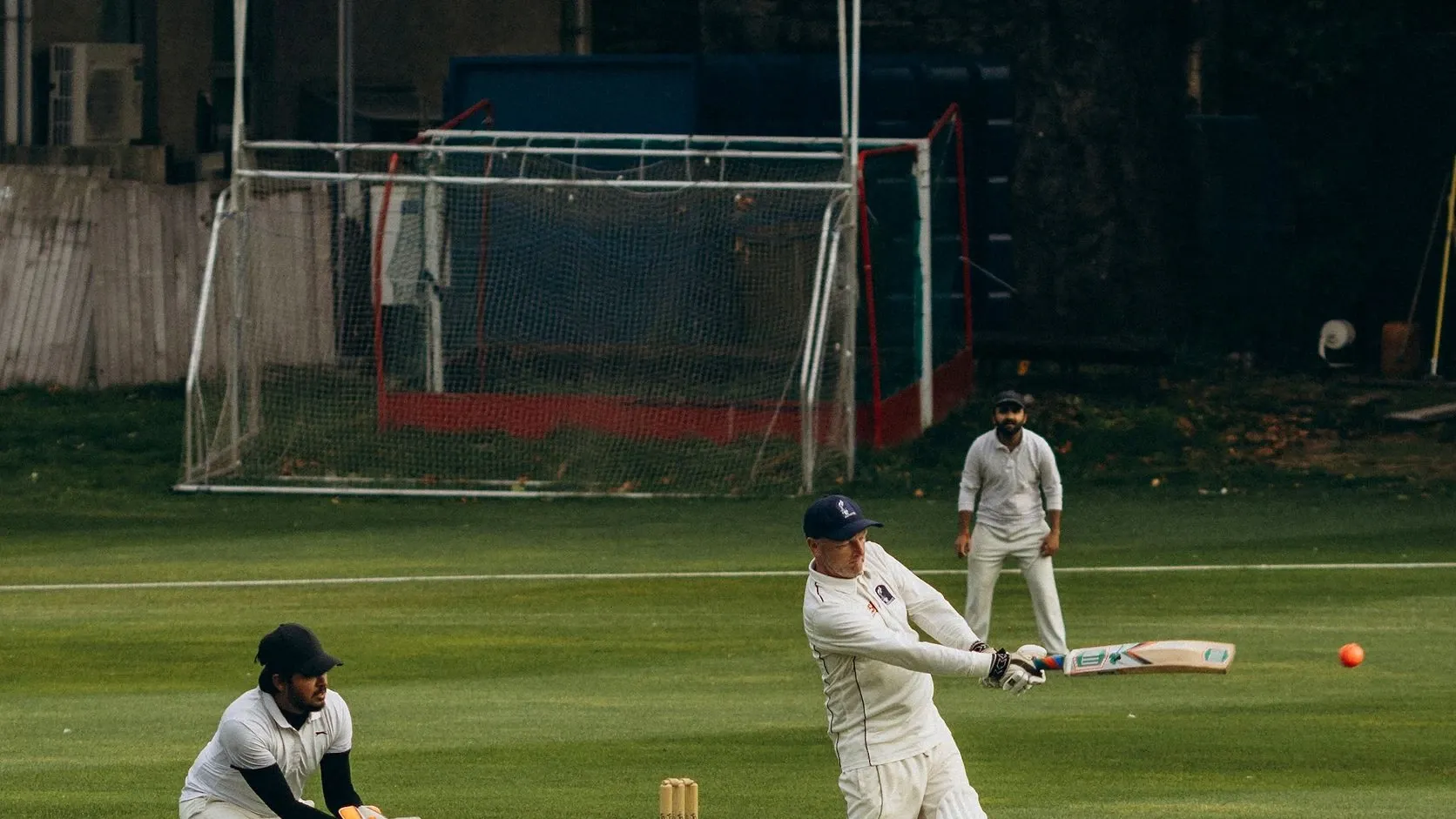 A batter plays a shot as the wicketkeeper follows the ball during a club cricket match